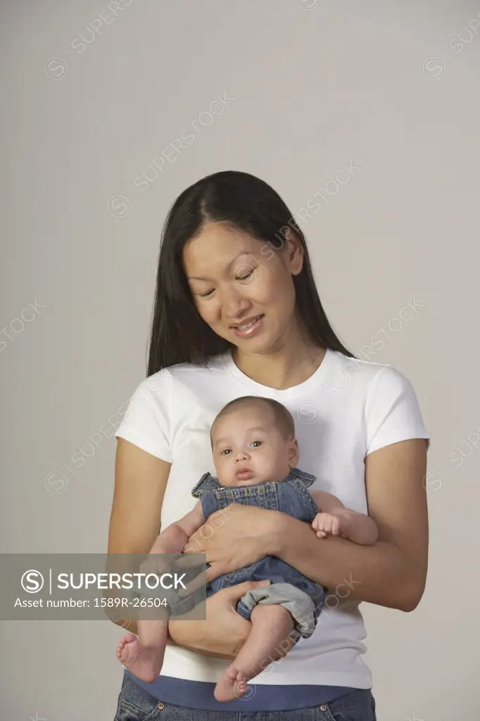 Asian mother holding baby in overalls
