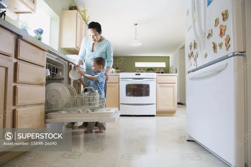Mother and young son putting dishes in dishwasher