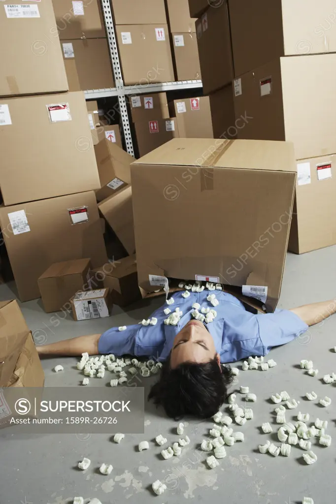 Male warehouse worker laying under fallen box with packing peanuts