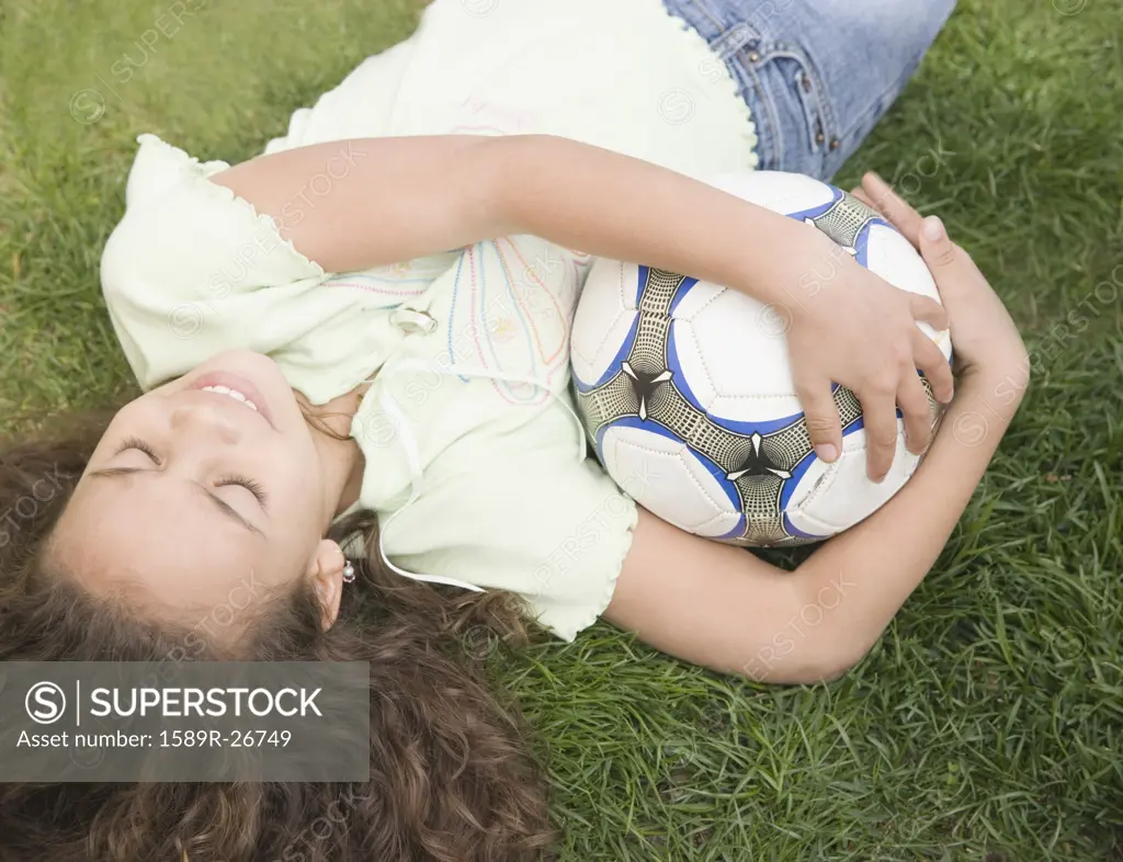 Young girl laying on ground with soccer ball