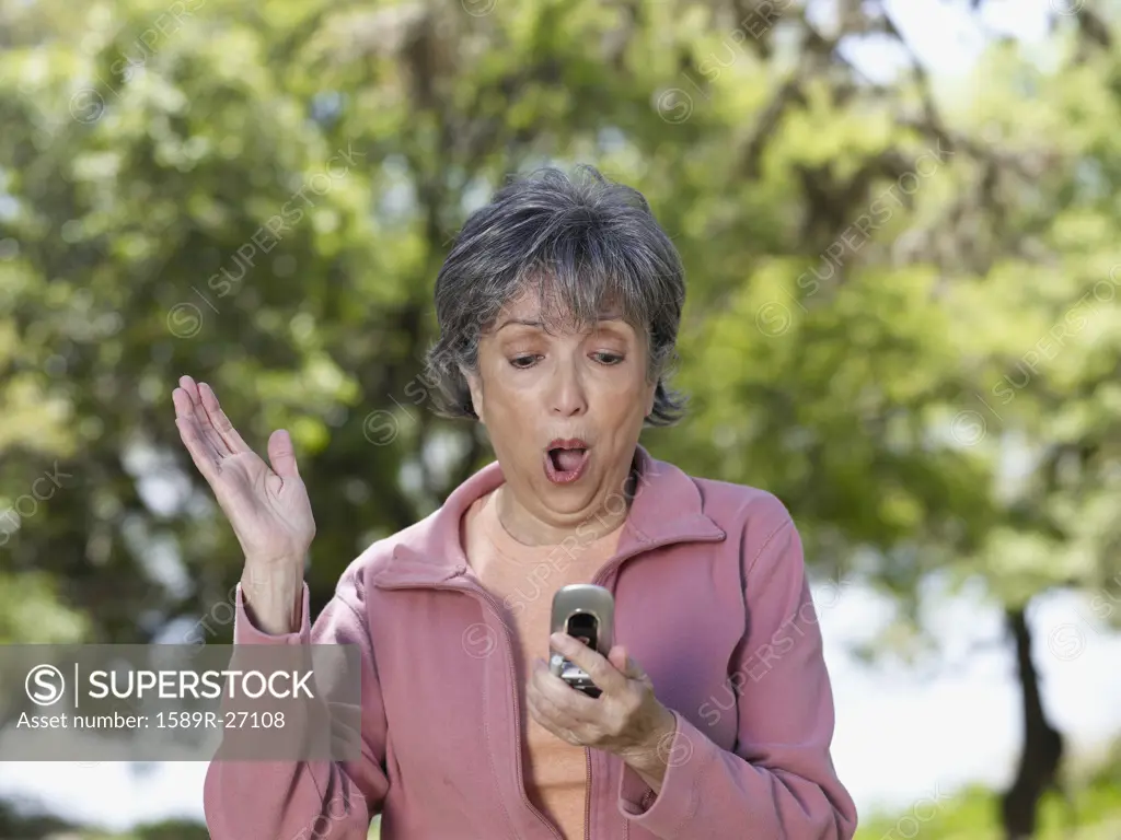 Senior Hispanic woman looking at cell phone with surprise