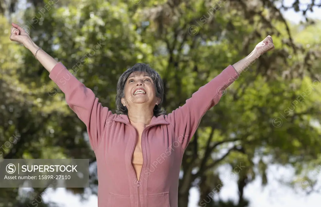 Senior Hispanic woman with arms raised outdoors