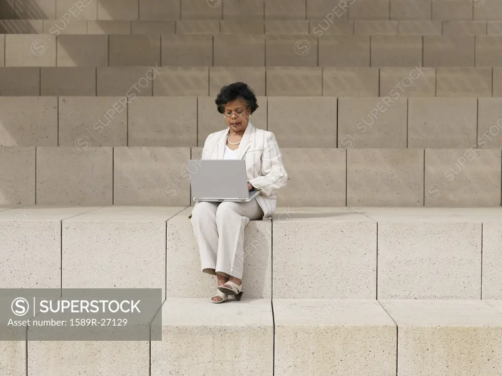 Senior African businesswoman using laptop on steps outdoors