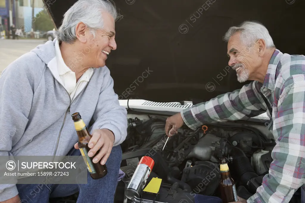 Two senior men working under hood of car