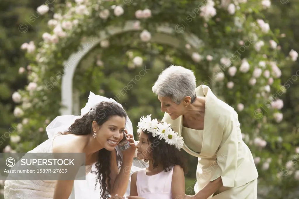 Hispanic bride using cell phone with young girl and mother