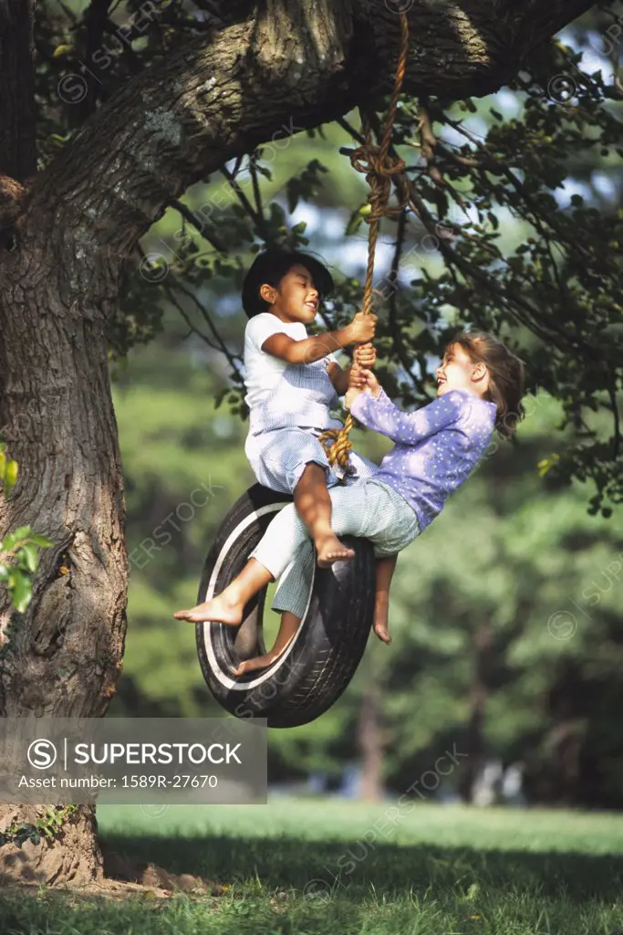 Two young girls swinging on tire swing