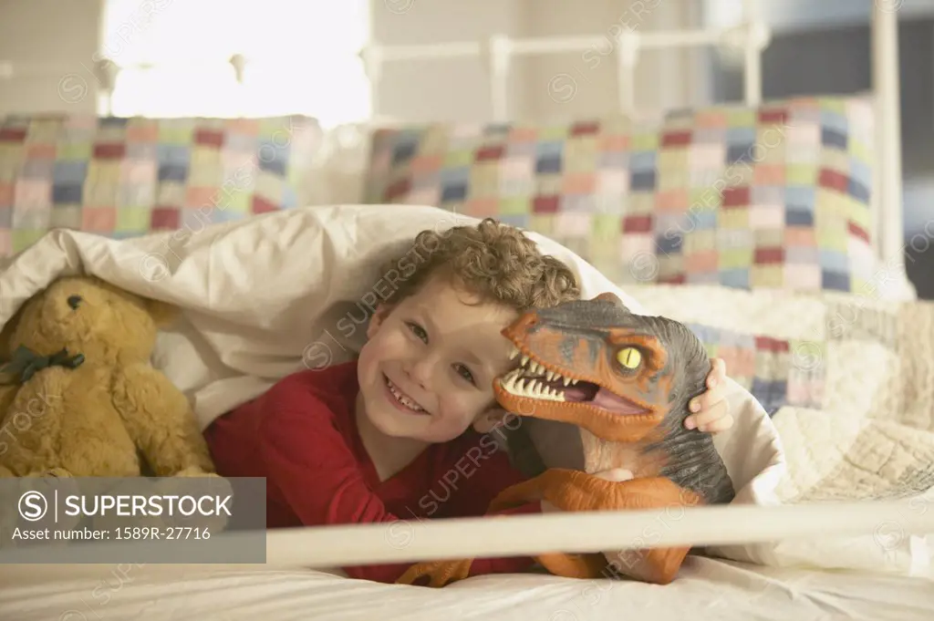 Young boy smiling in bed with toy dinosaur