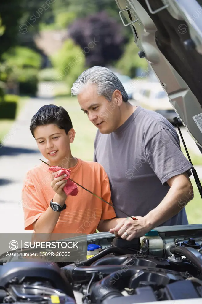 Hispanic father and son checking oil in car