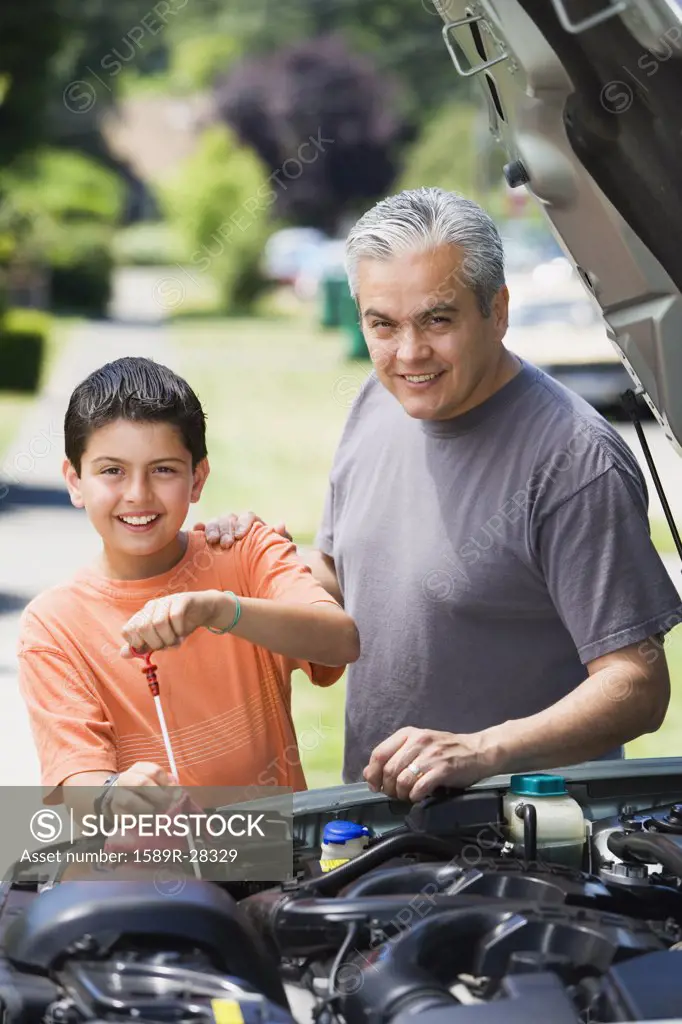 Hispanic father and son checking oil in car