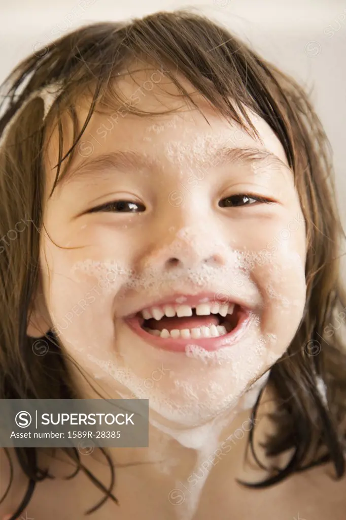 Close up of young girl smiling with soap suds on face