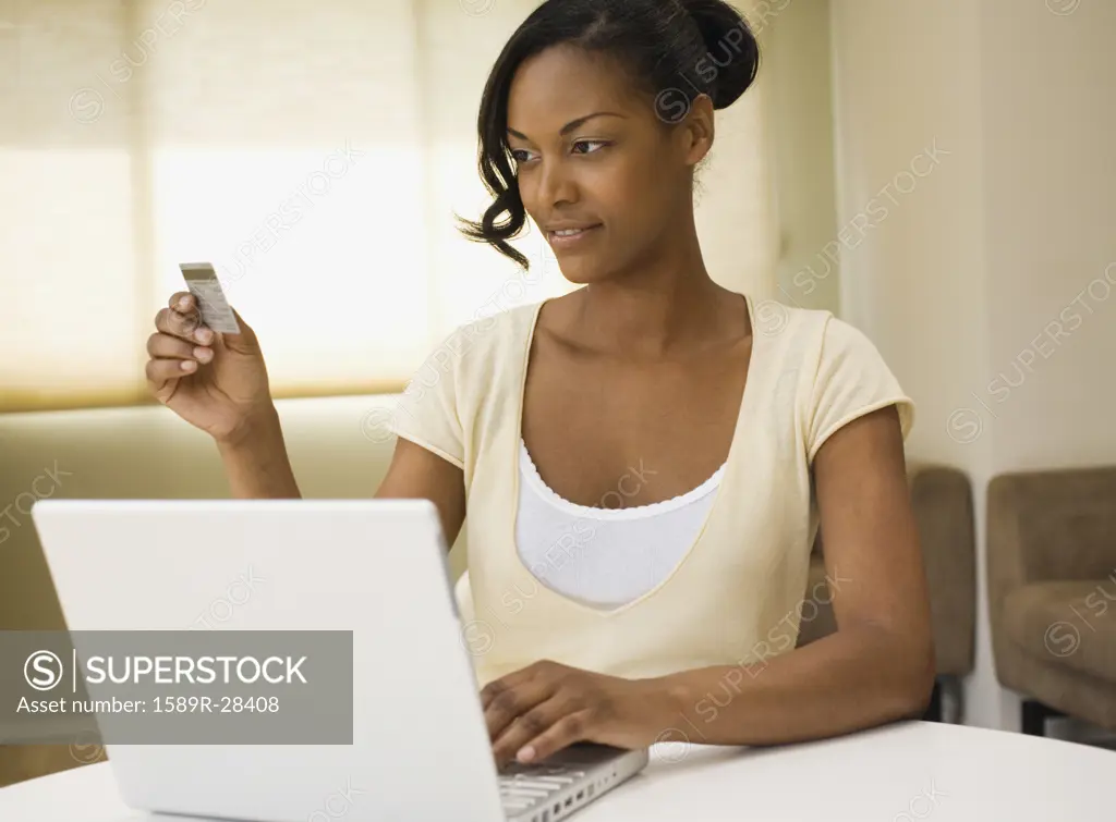 African woman using credit card and laptop indoors