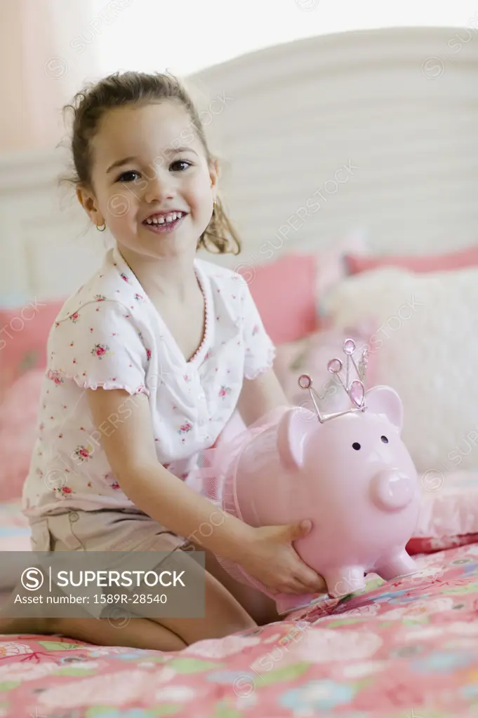 Young girl with piggy bank on bed