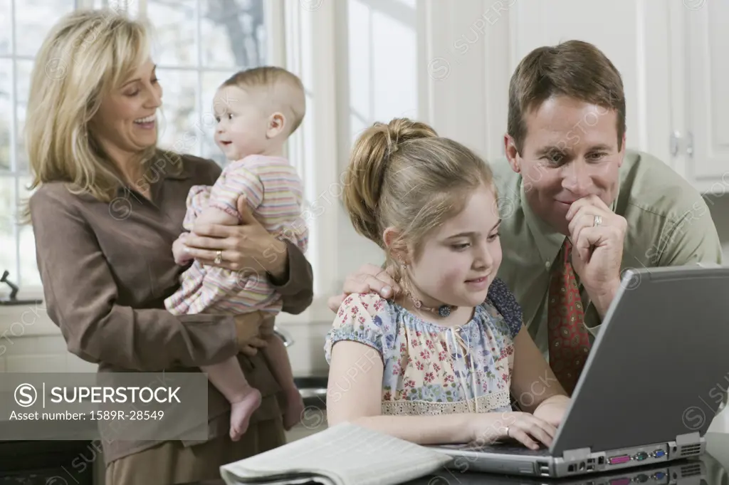 Father helping daughter use laptop while mother holds baby