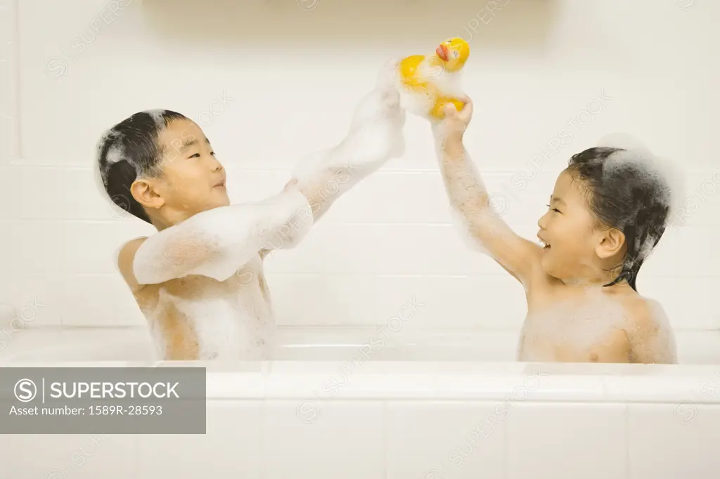 Young Asian sister and brother playing with rubber duck in bathtub
