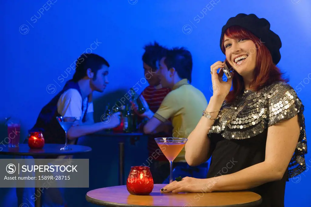 Woman with cocktail and cell phone standing at nightclub table