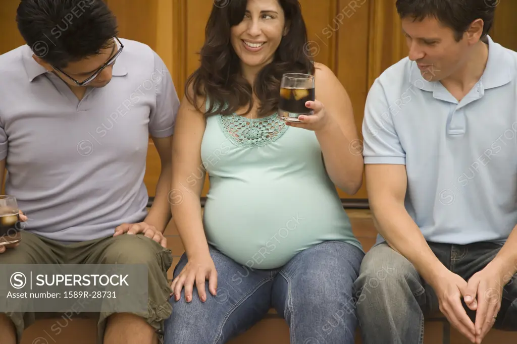 Pregnant woman sitting next to two men looking at her belly
