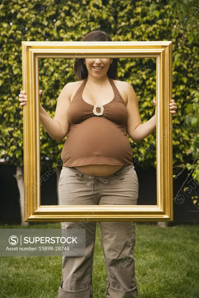 Pregnant woman holding up picture frame outdoors