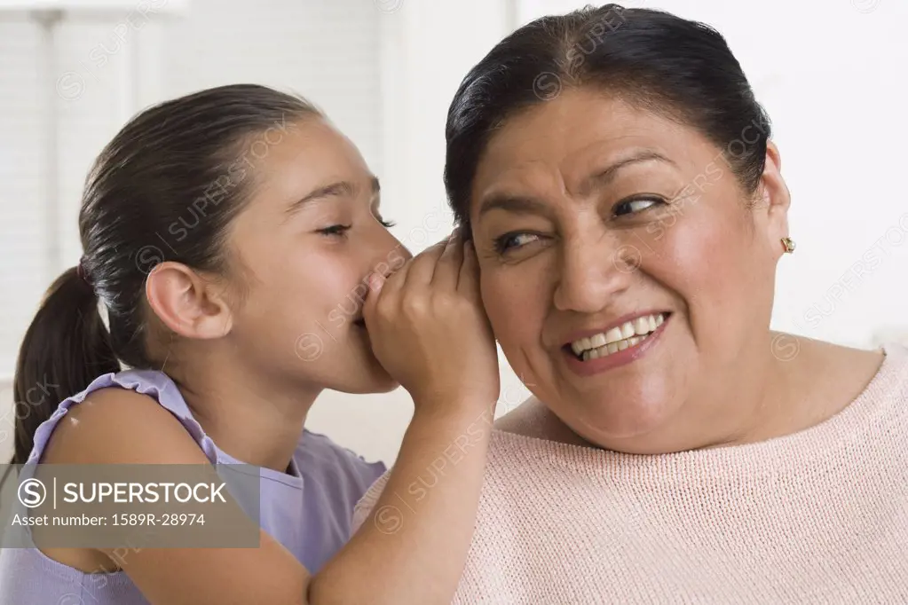 Hispanic girl whispering in grandmother's ear