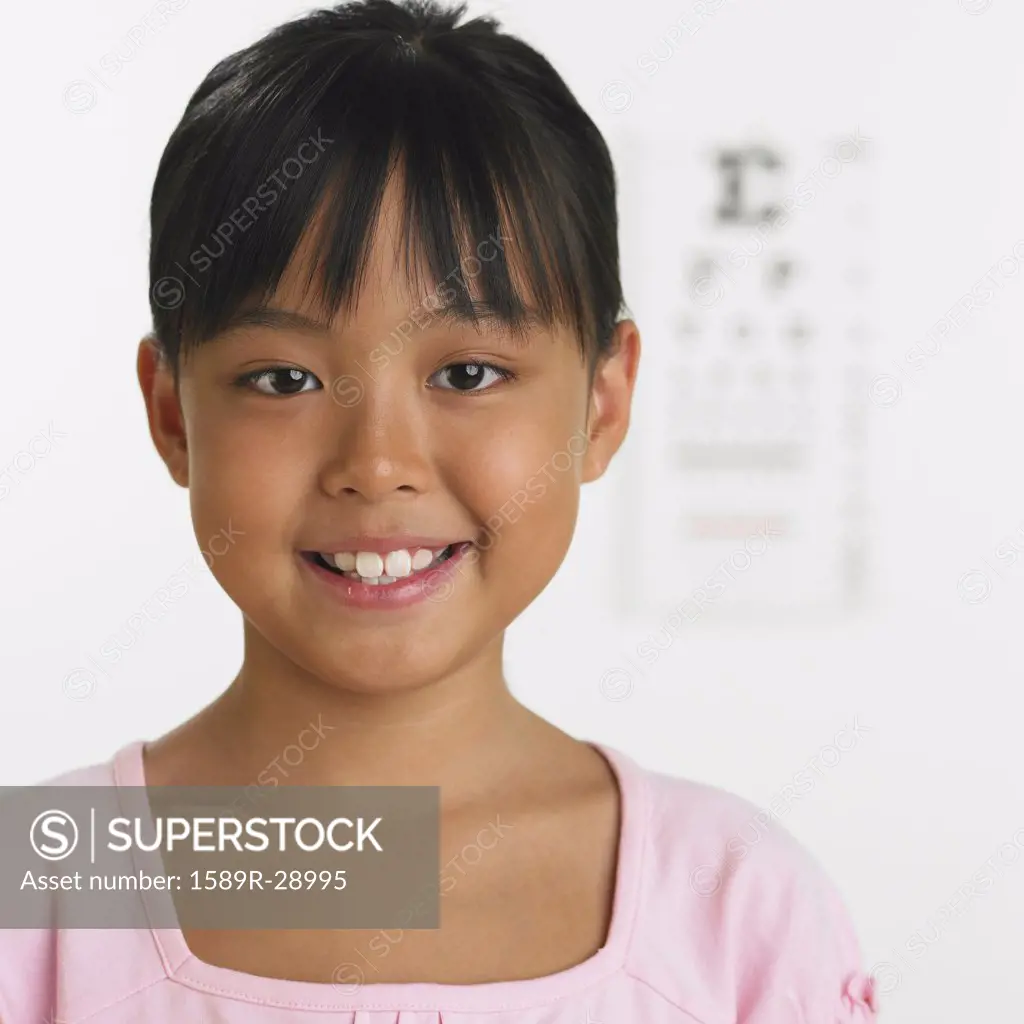 Young girl smiling with eye chart in background