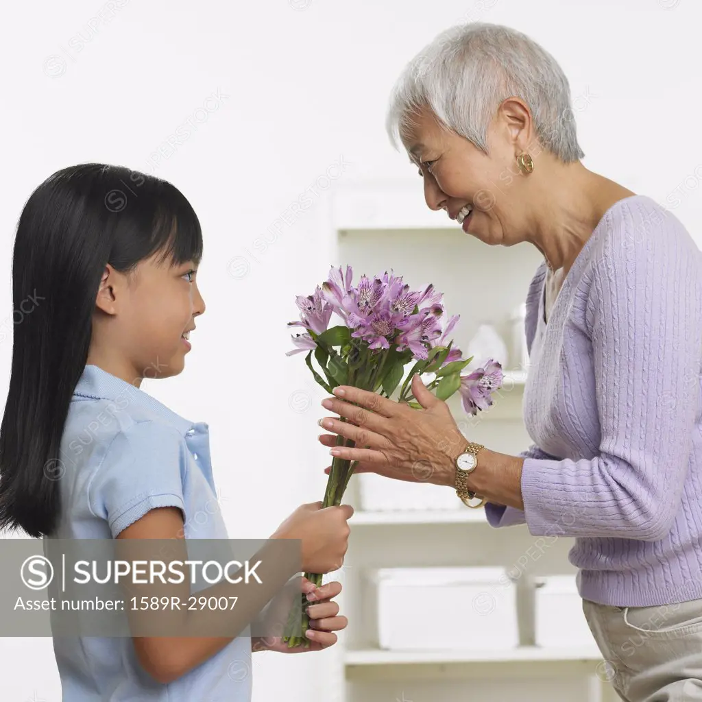 Asian girl giving grandmother bouquet of flowers