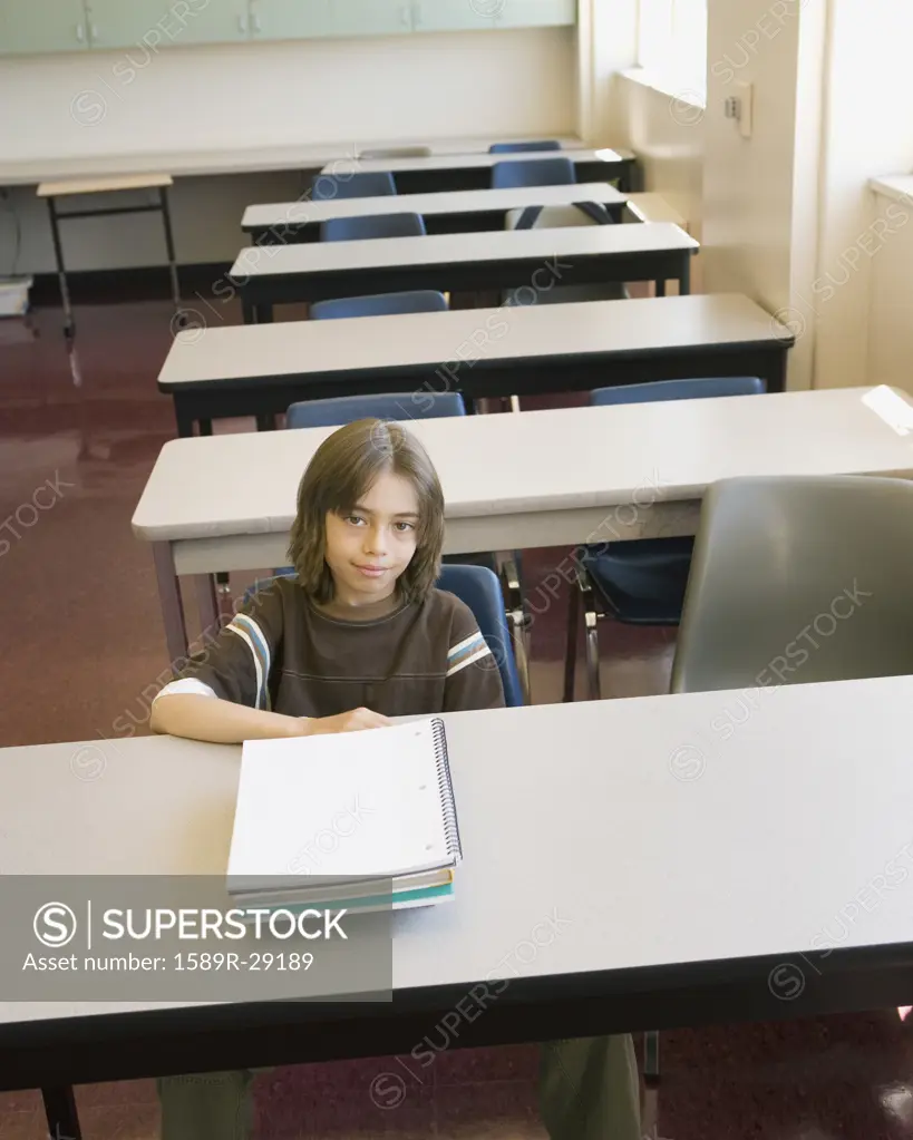 Boy sitting at desk in empty classroom