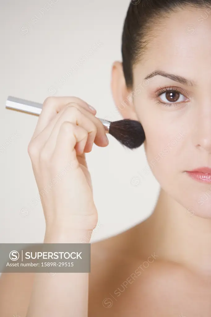 Close up studio shot of Hispanic woman using make up brush
