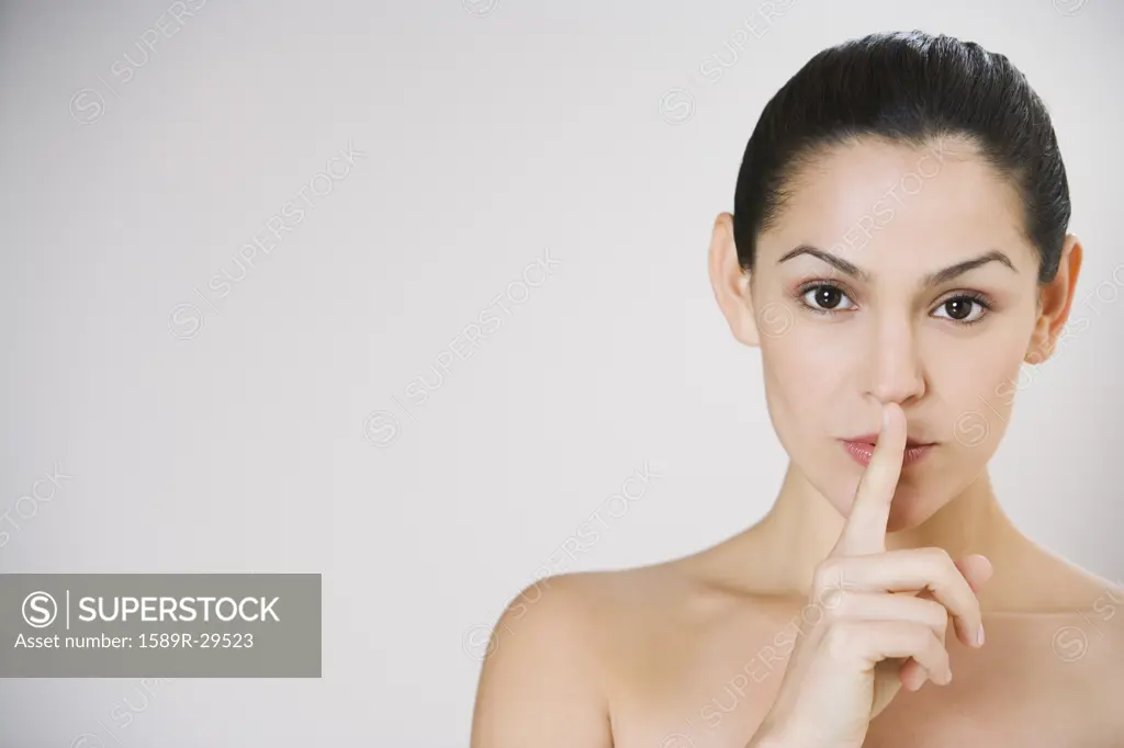 Close up studio shot of Hispanic woman with index finger up to lips