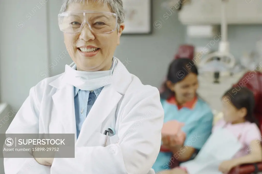 Senior Asian female dentist with assistant and patient in background