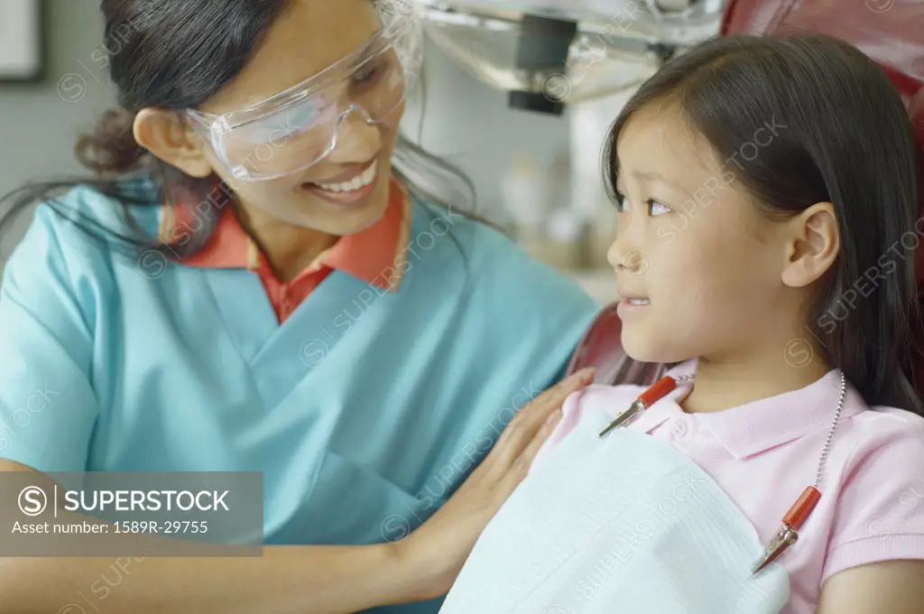 Indian female dental assistant smiling at young Asian female patient