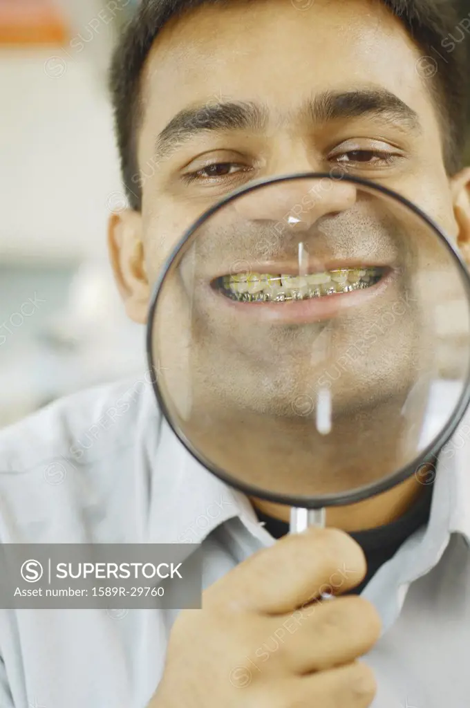 Indian man holding up magnifying glass to his teeth with braces