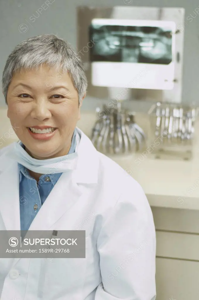 Senior Asian female dentist smiling next to x-rays