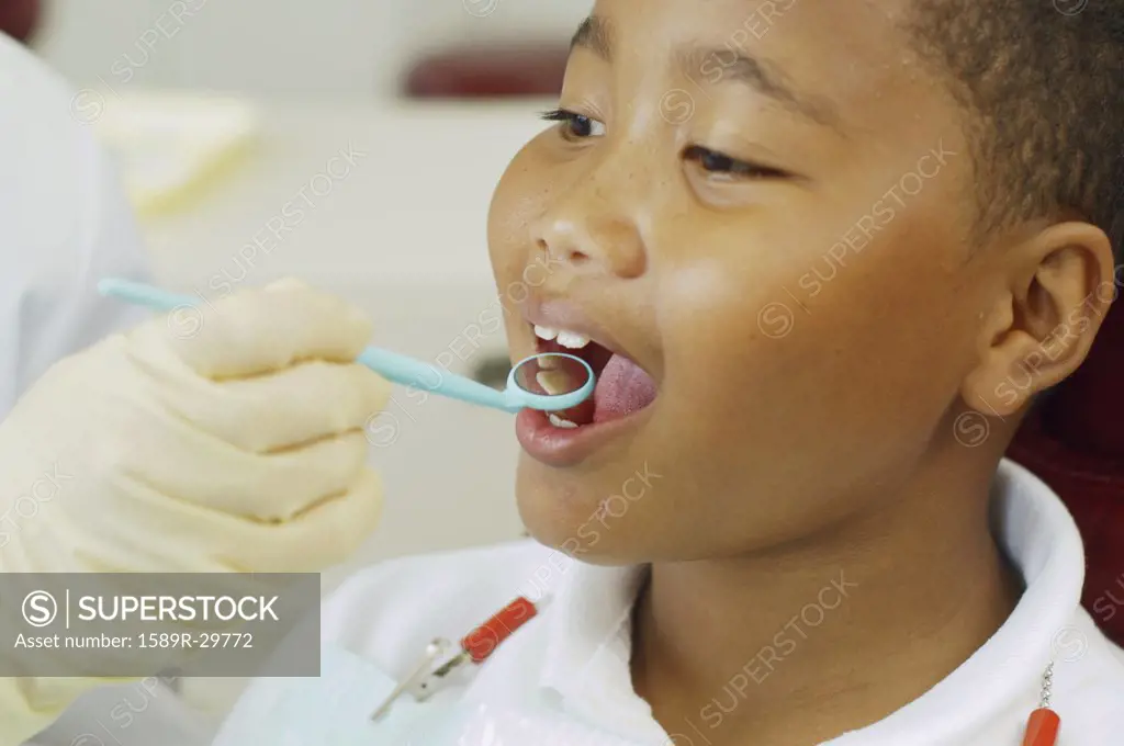 Dentist's hand holding dental mirror in boy's mouth