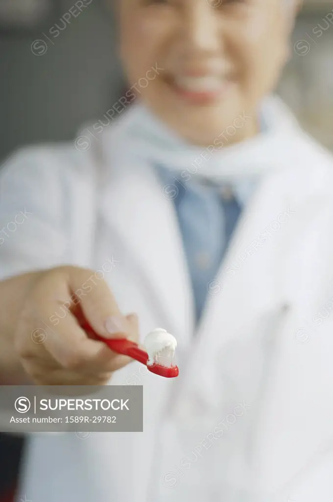 Female dentist holding out toothbrush with toothpaste