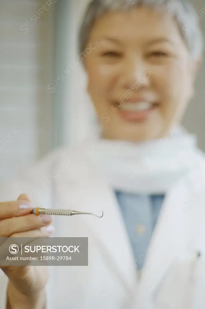Senior Asian female dentist holding up dental tool