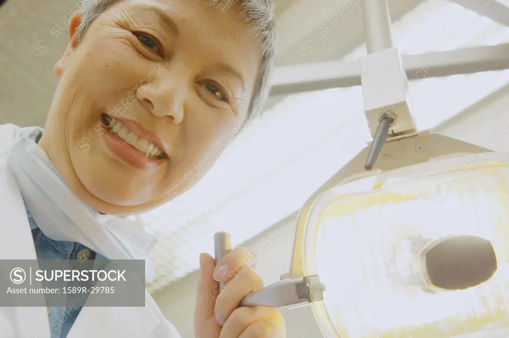 Senior Asian female dentist adjusting light