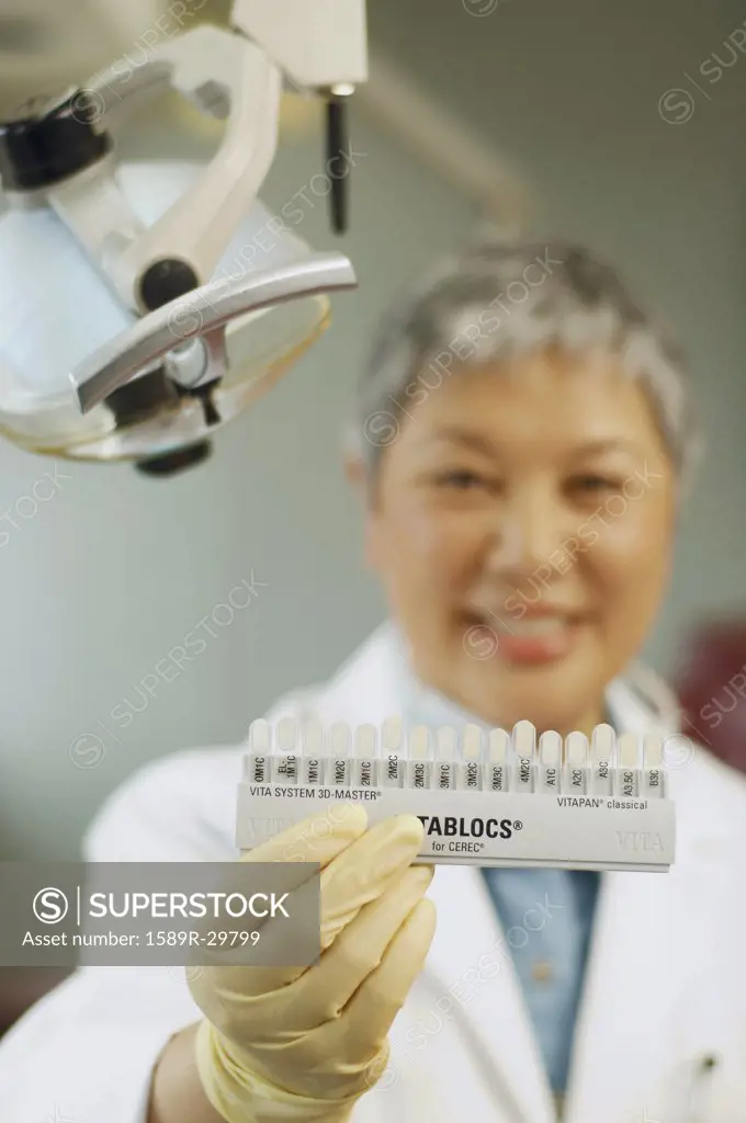 Senior Asian female dentist holding tooth color samples