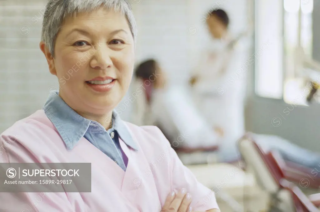 Senior Asian female dental assistant with dentist and patient in background