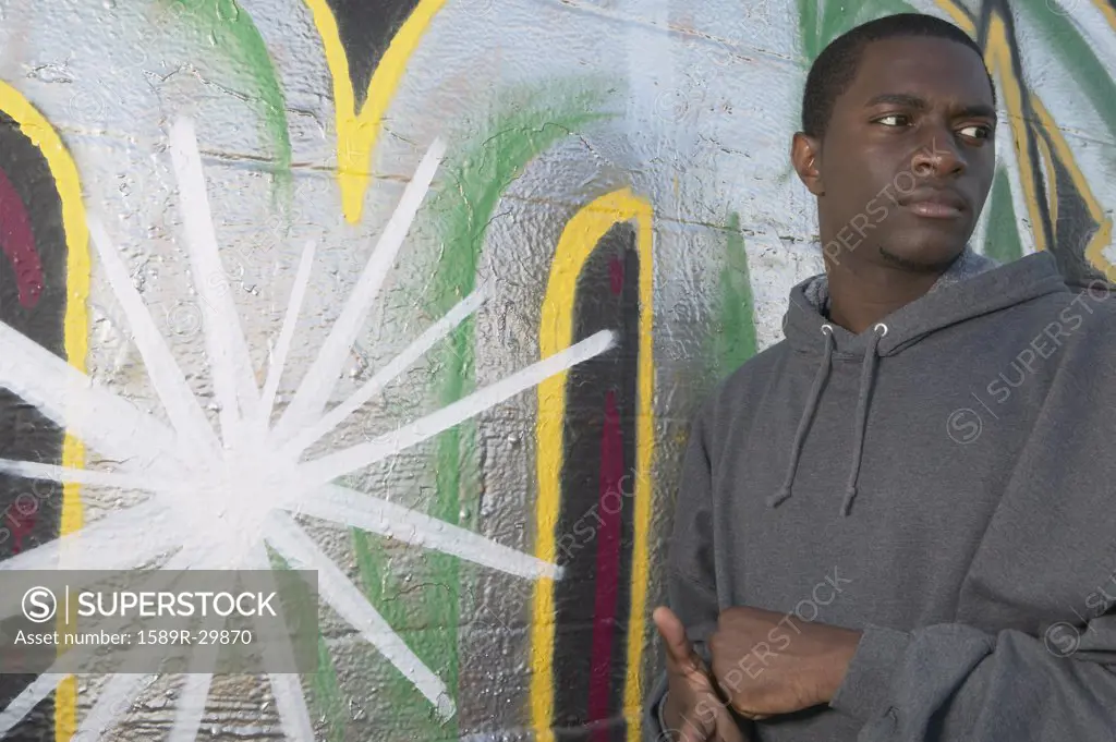 Young African man leaning on graffitied wall