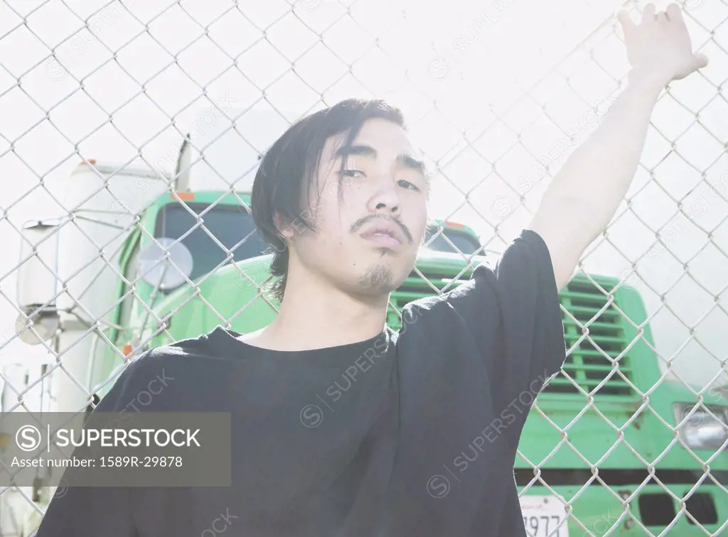 Young Asian man leaning against metal fence