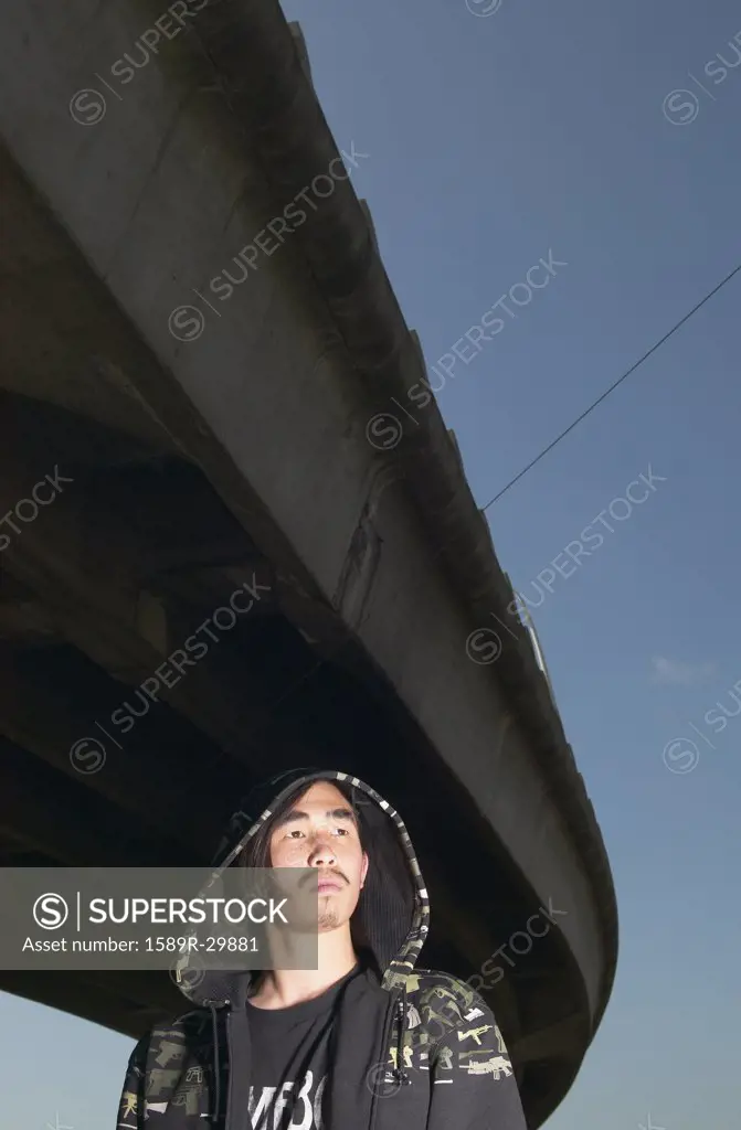 Young Asian man standing under raised highway