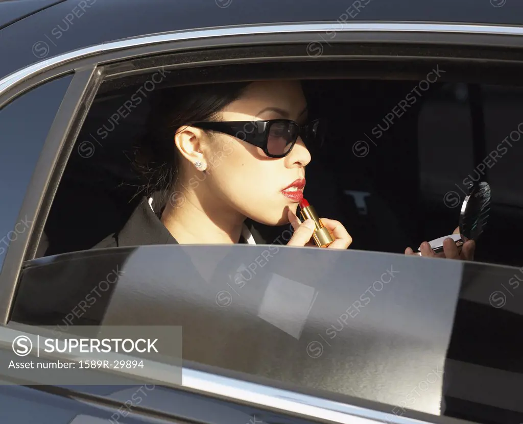 Asian woman applying lipstick in backseat of car