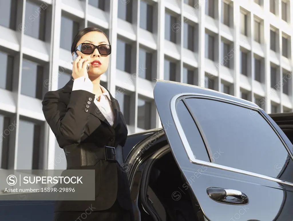 Asian businesswoman using cell phone next to car
