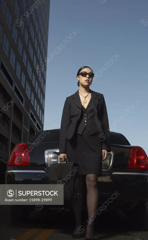 Asian businesswoman with briefcase standing at back of car