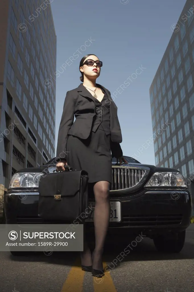 Asian businesswoman with briefcase standing at front of car