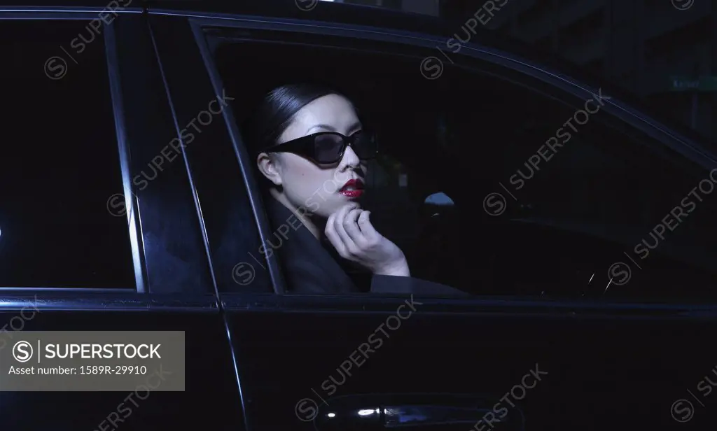 Asian woman sitting in car wearing sunglasses