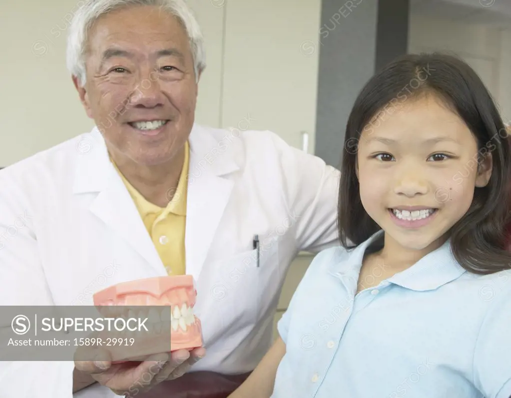 Senior Asian male dentist showing model of teeth to young patient