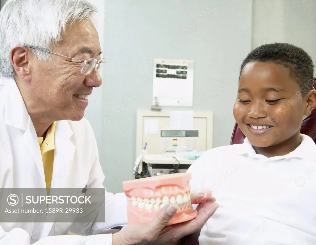Senior Asian male dentist showing tooth model to young male patient