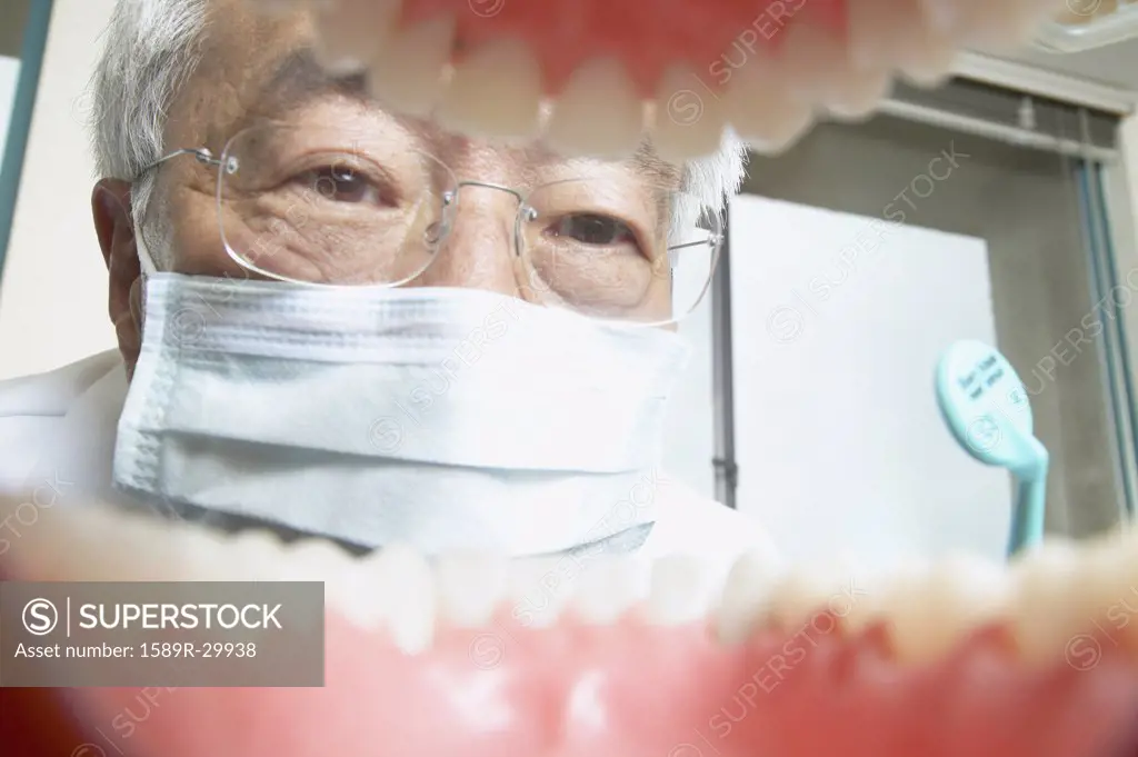 Shot from mouth looking out at senior Asian male dentist