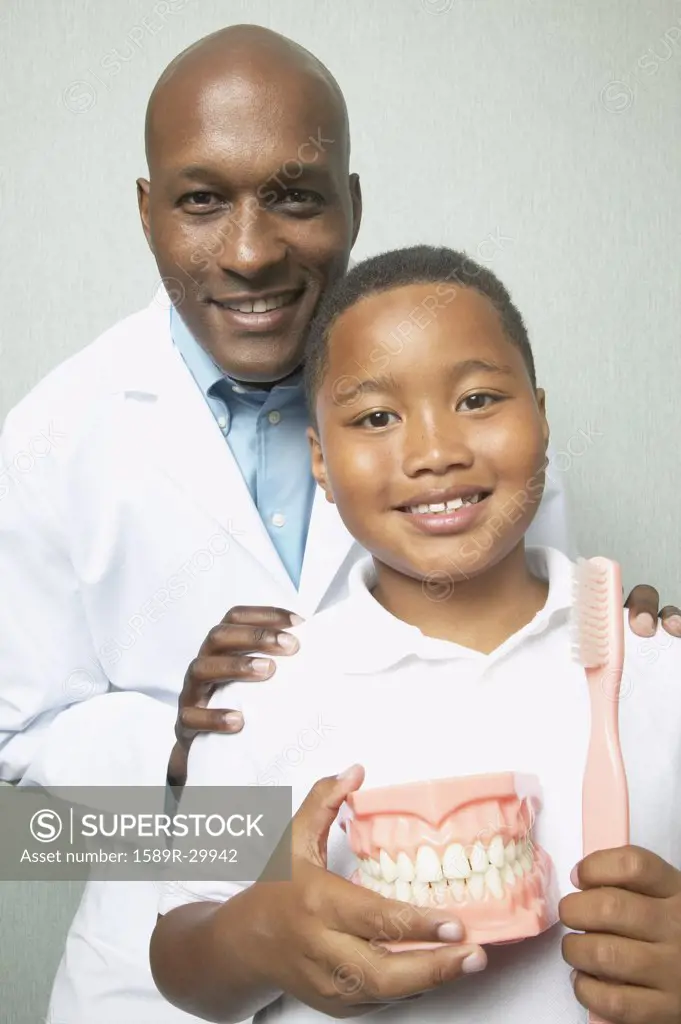 African male dentist with boys holding toothbrush and model of teeth