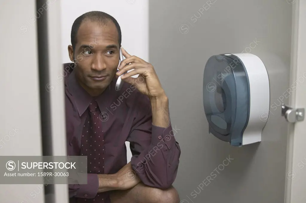 African businessman using cell phone in restroom stall